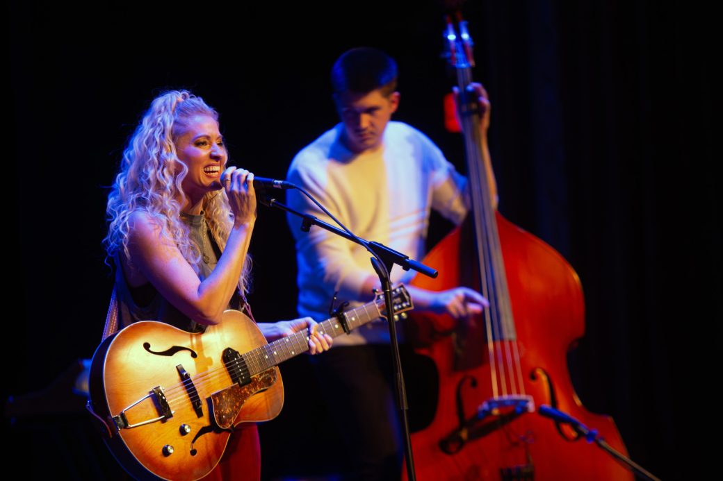 Woman singing at Conctpalooza and playing acoustic guitar