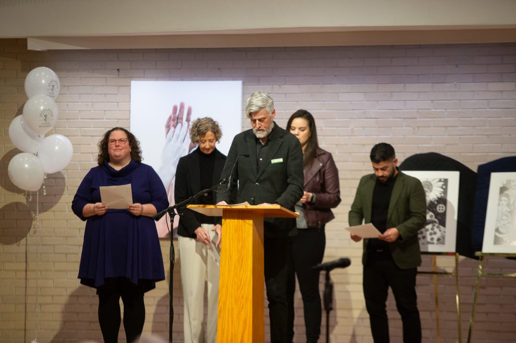 man doing a speech at stage's pulpit and other people at the stage reading their papers