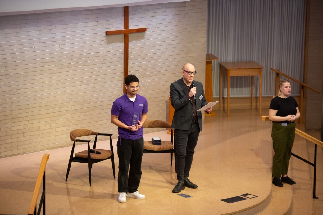 junior of the Goshen college Fernando Daza the student Vibrant Leader Award and a man giving a speech at the stage