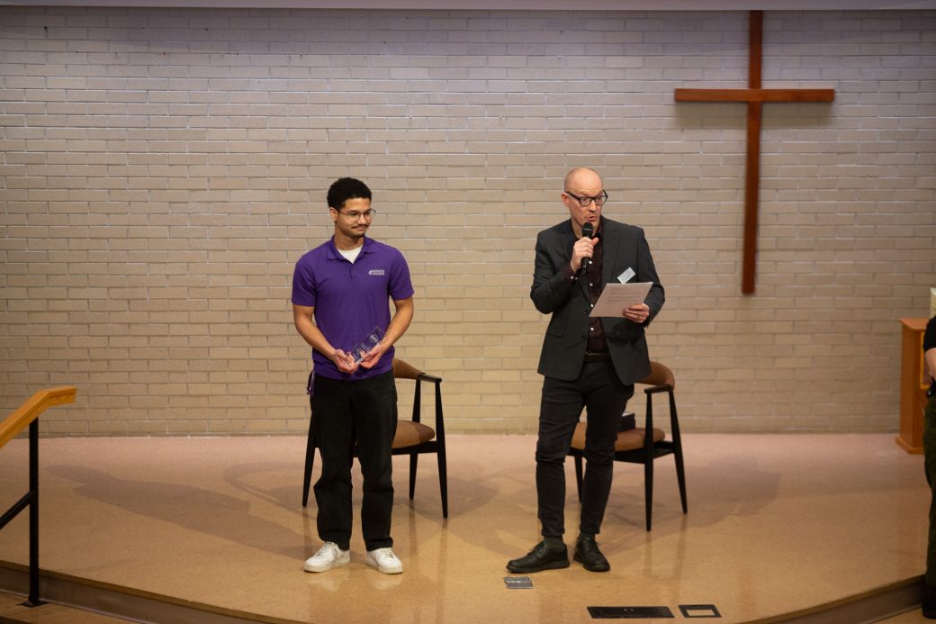 junior of the Goshen college Fernando Daza the student Vibrant Leader Award and a man giving a speech at the stage