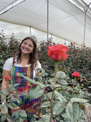 student smiling behind red rose