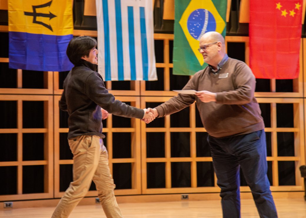 Two men handshaking on the stage at International Student Club Coffeehouse 2023