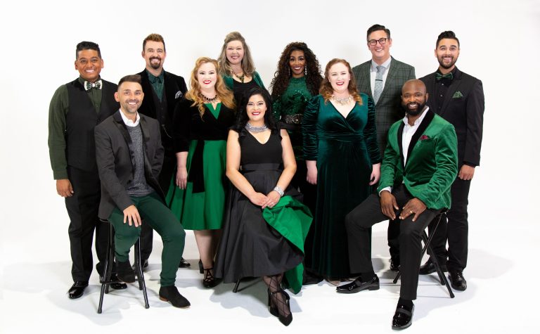 A group of about ten people dressed in black and dark green smiles for a photo.