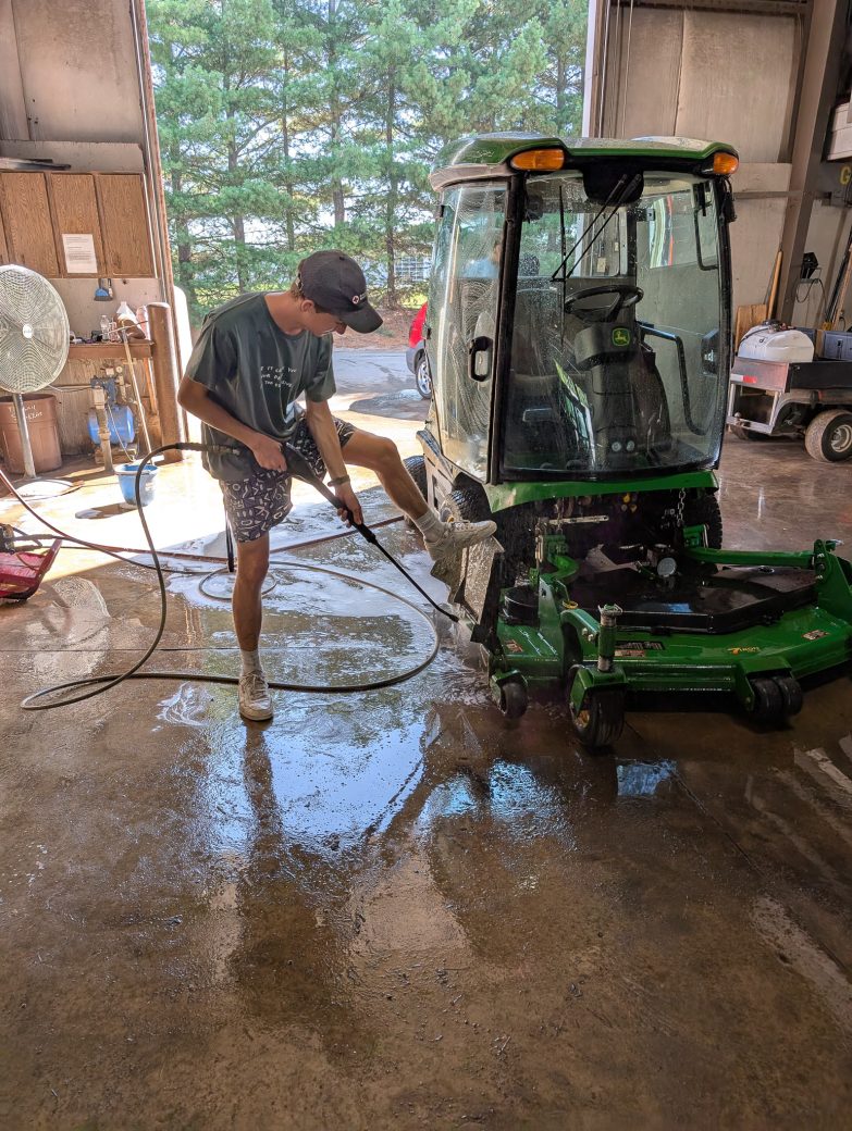 A boy washing a agricultural machinery