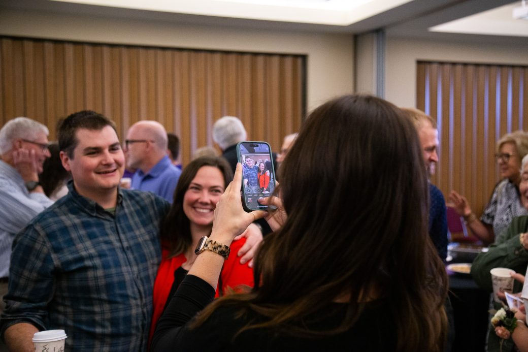 A woman taking a photo of a man and a woman hugging at 2025 Alumni Awards Convocation