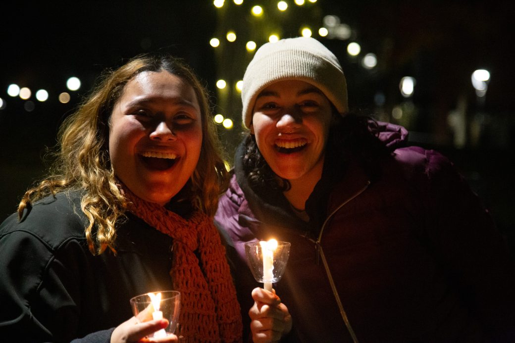 Two women with lit candles smiling at tree lighting.