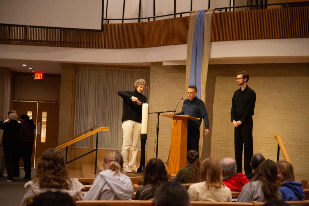Campus minister Jen Shenk lights a candle on stage at the ceremony
