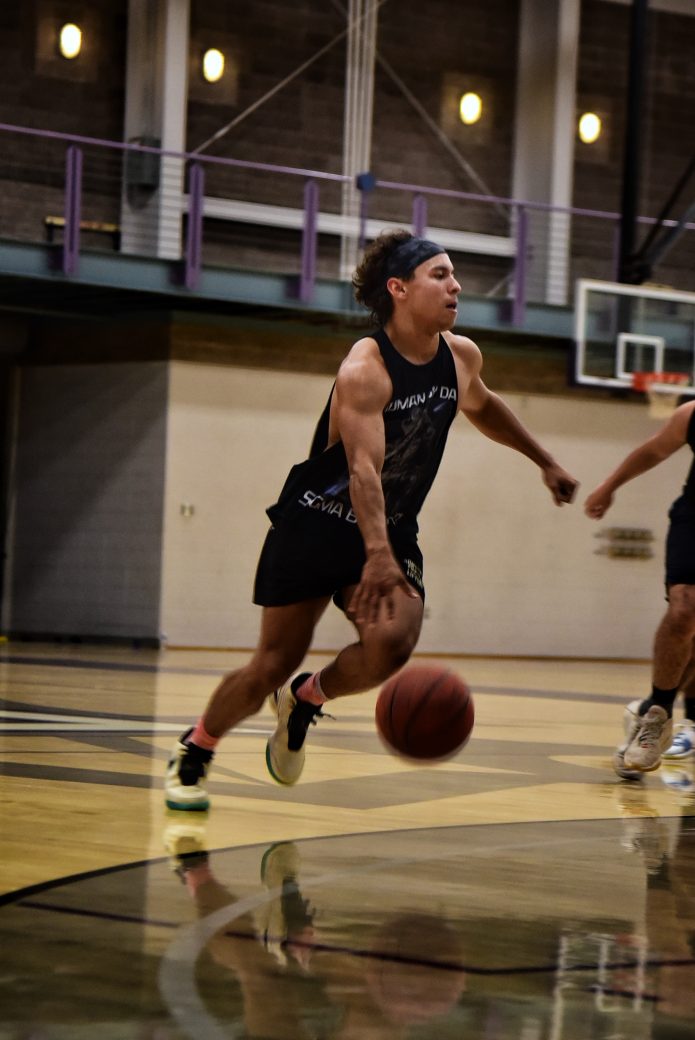 Male player in black tank dribbles with ball on court