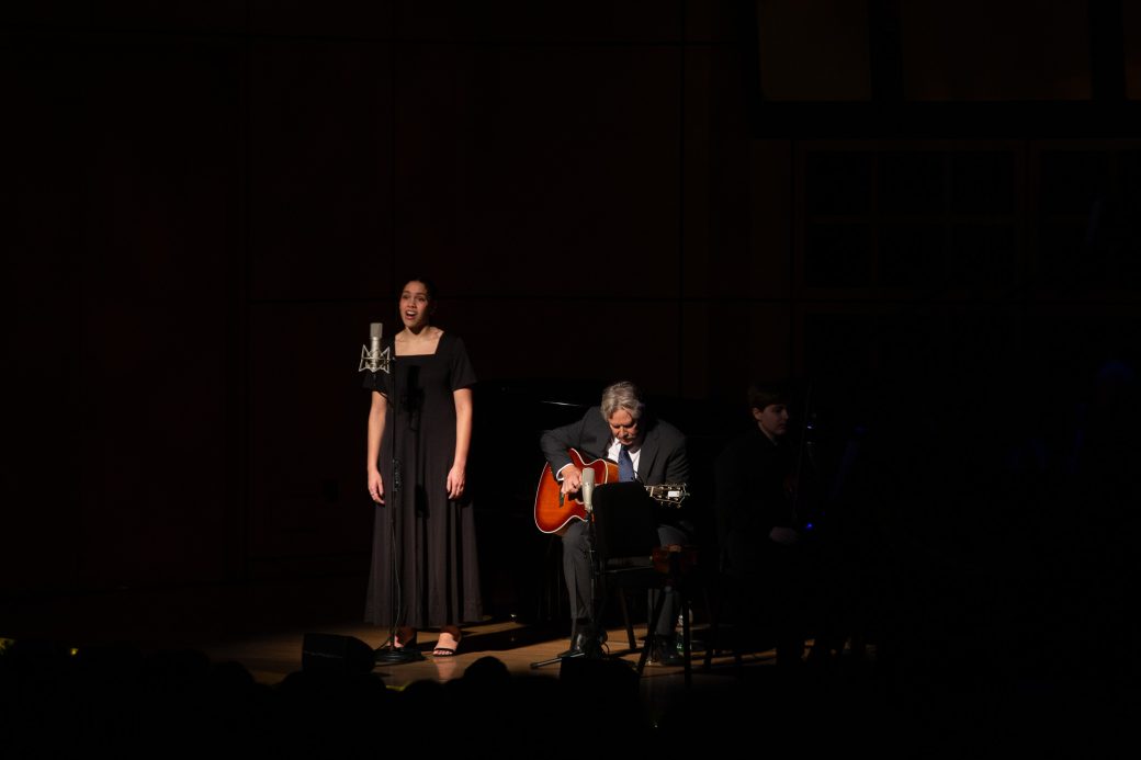 Man plays guitar next to student singing