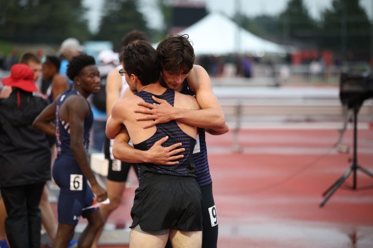 Two male track athletes embrace in celebration.