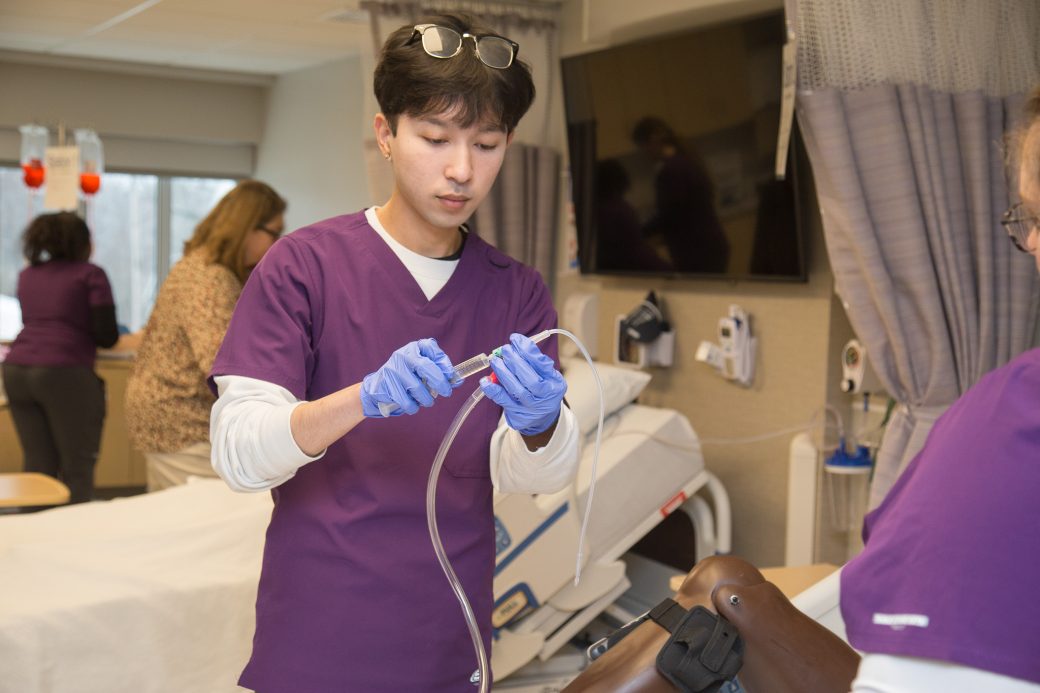 A student in scrubs working with an IV