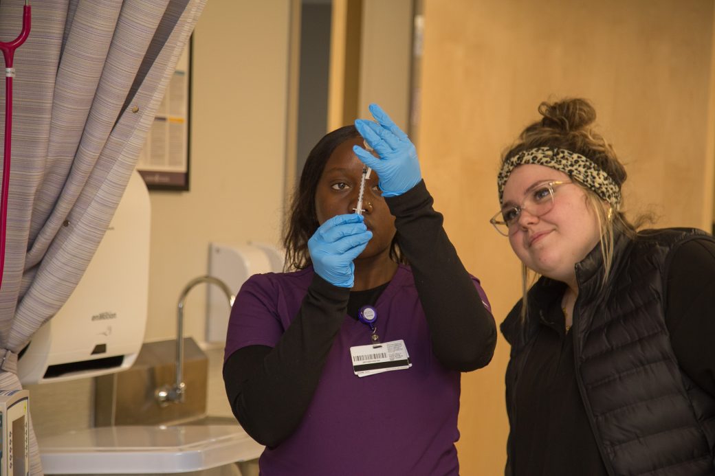 Two people, teaching how to fill a syringe