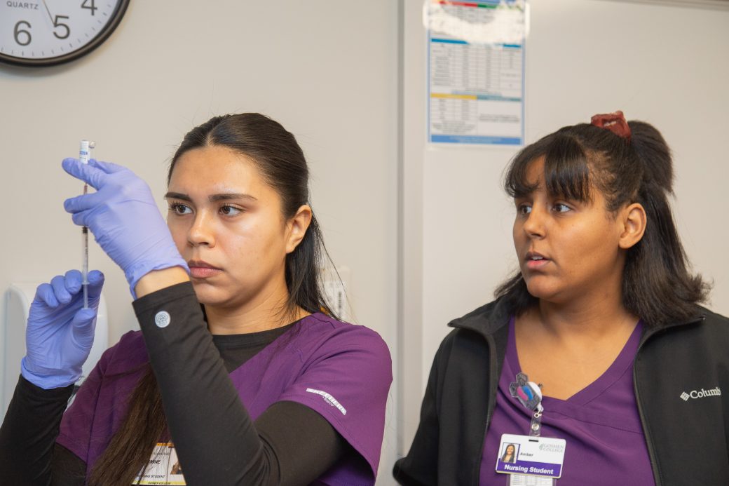 Two people in scrubs, working on filling a syringe
