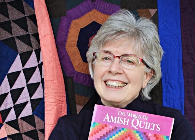 Rebecca Haarer holding a book and smiling in front of quilts