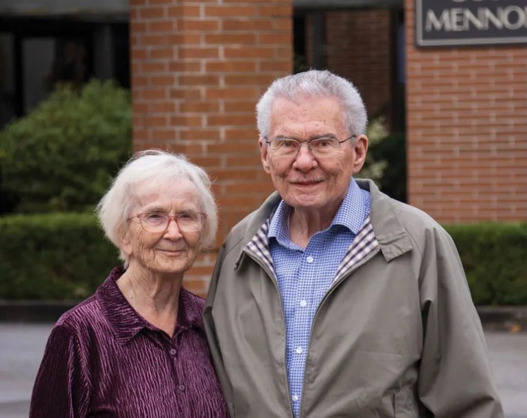 two people smiling in front of a brick building