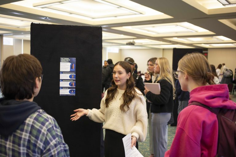 student explaining a poster to other people with lots of people around