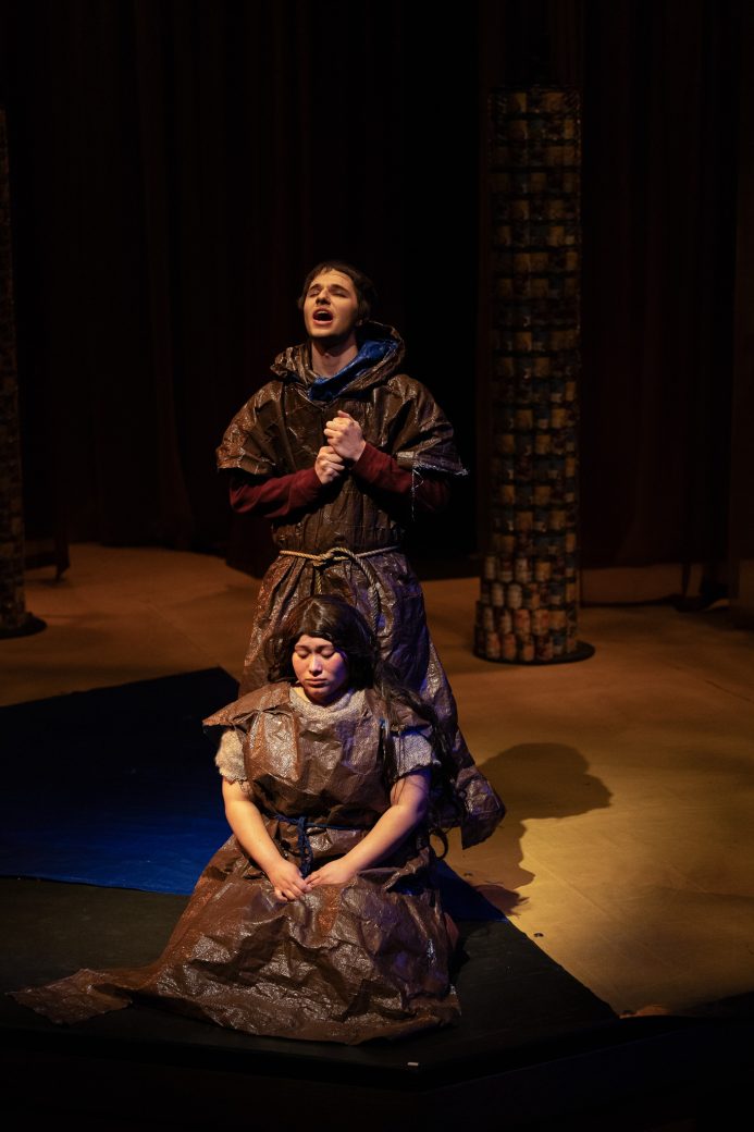 actor kneeling with a man praying behind her