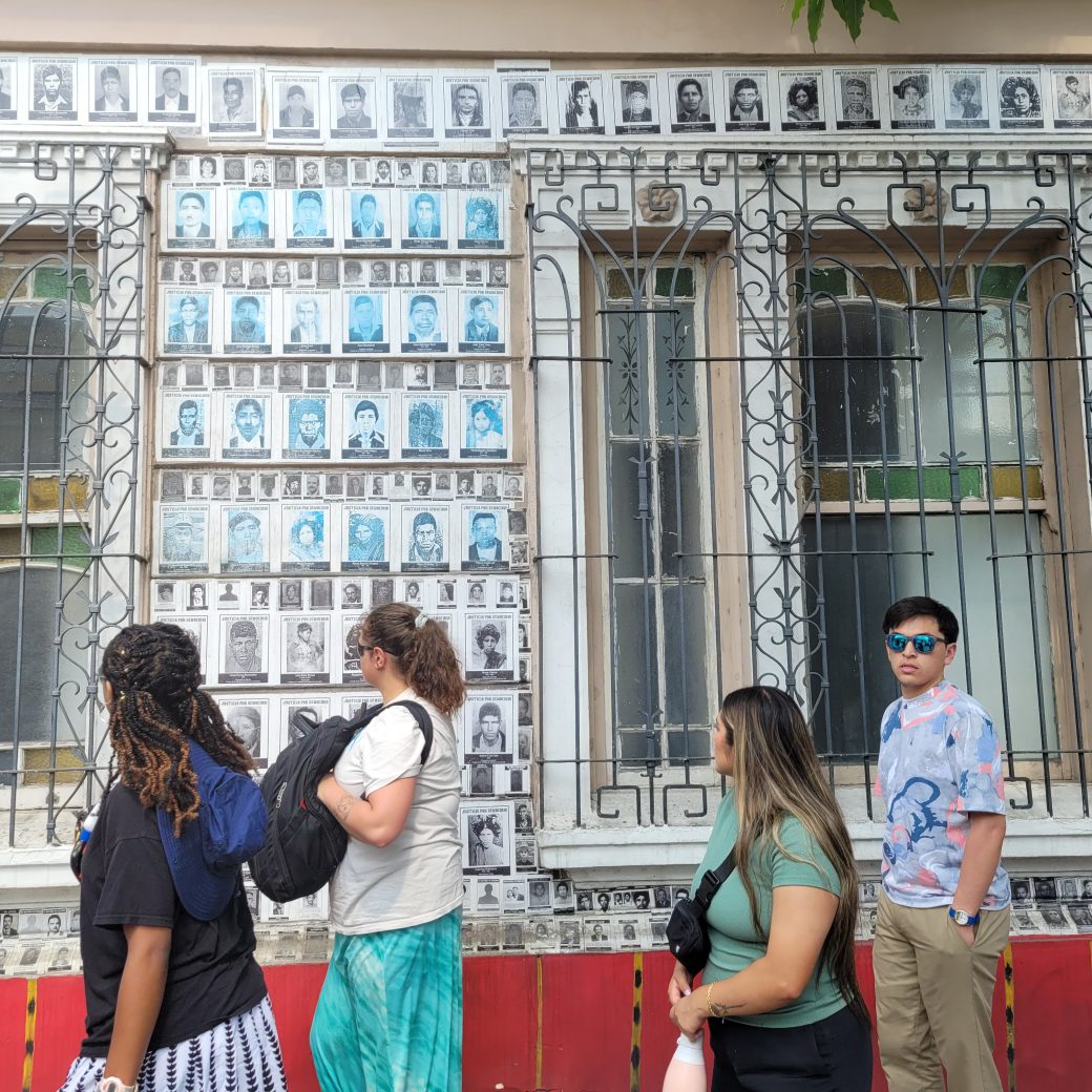 People walking in front of a building covered with portraits.