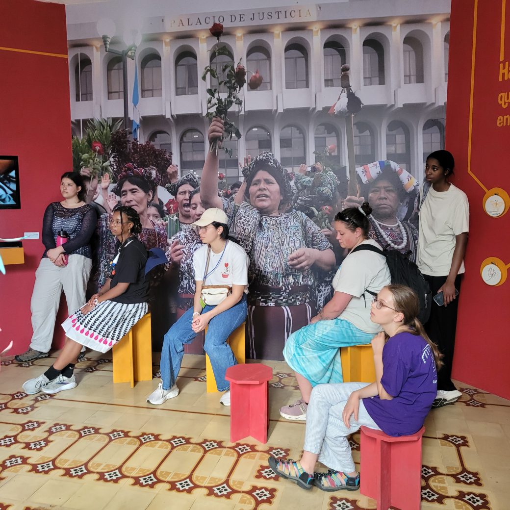 Individuals sitting in a museum exhibit, in front of a large photo.