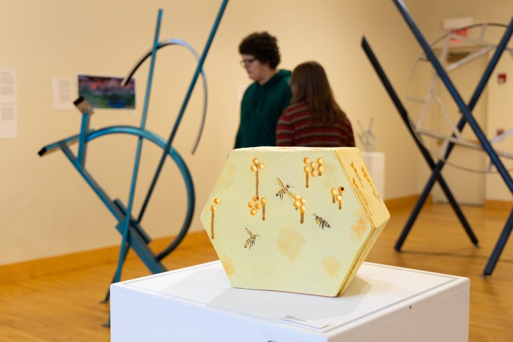 CLose up of honeycomb artwork with students behind it talking
