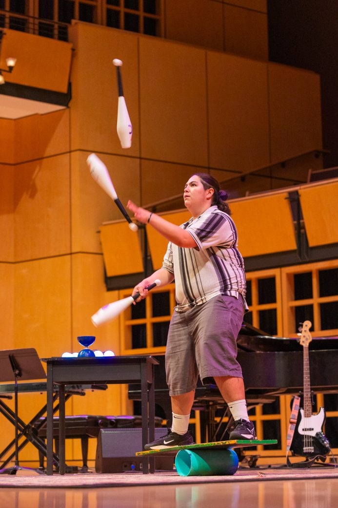 Student juggling with pin balls while balancing on a balance board