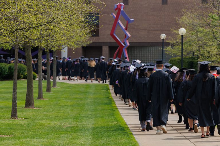Graduates walk on sidewalk toward the Roman Gingerich Recreation-Fitness Center