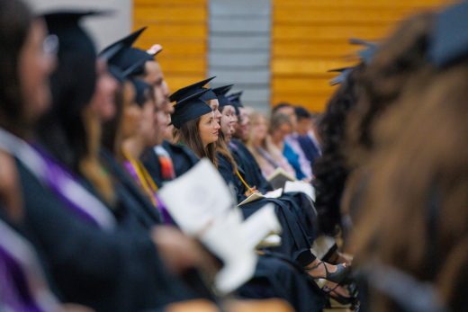 students in graduation caps and gowns sitting in crowd