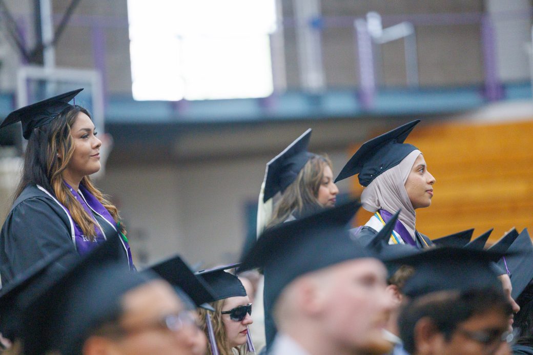 Several graduates standing up out of crowd of graduates
