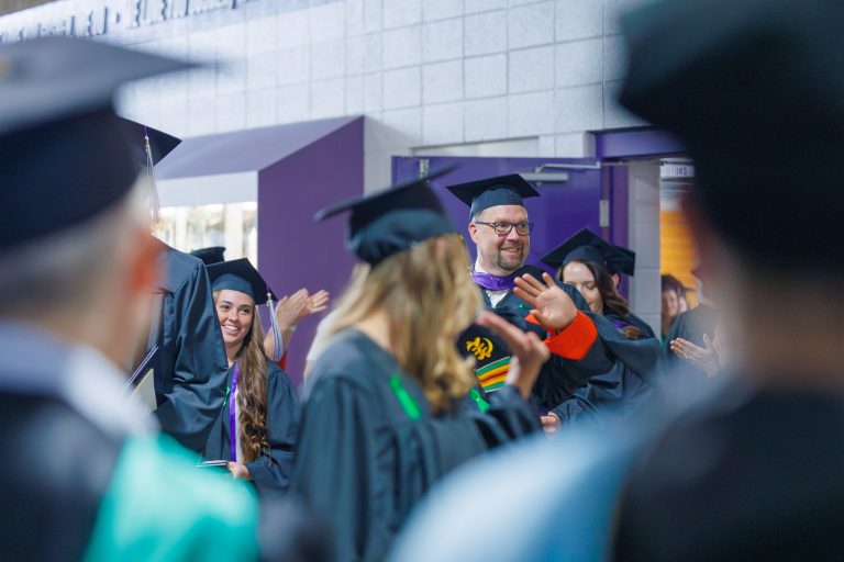 Graduates leaving ceremony as faculty and staff line walkway applauding