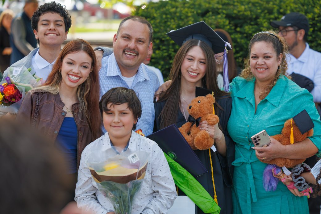 Graduate holding stuffed teddy bear with family
