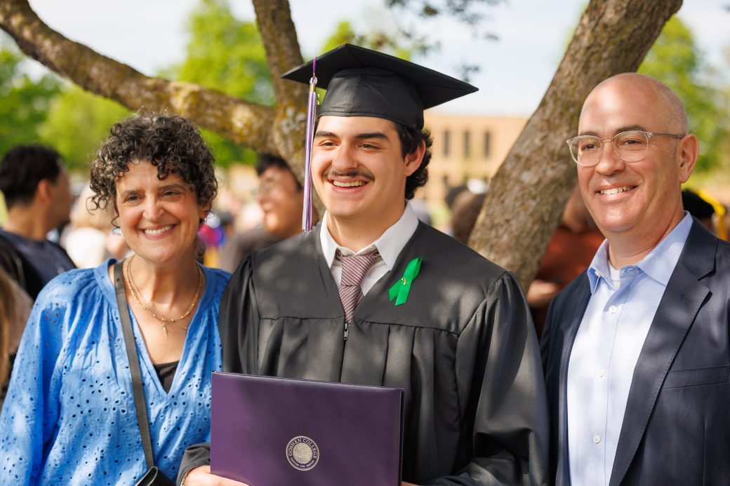 Graduate under a tree posed with family and diploma