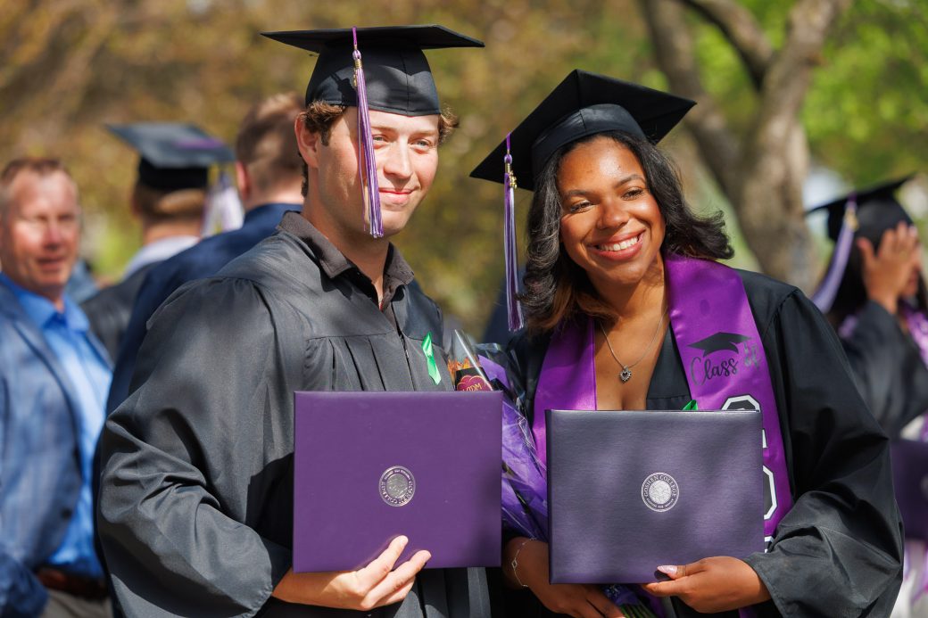 Two graduates smiling holding their diplomas