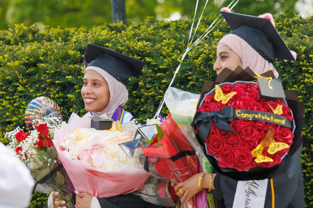 Two graduates holding huge boquets of flowers