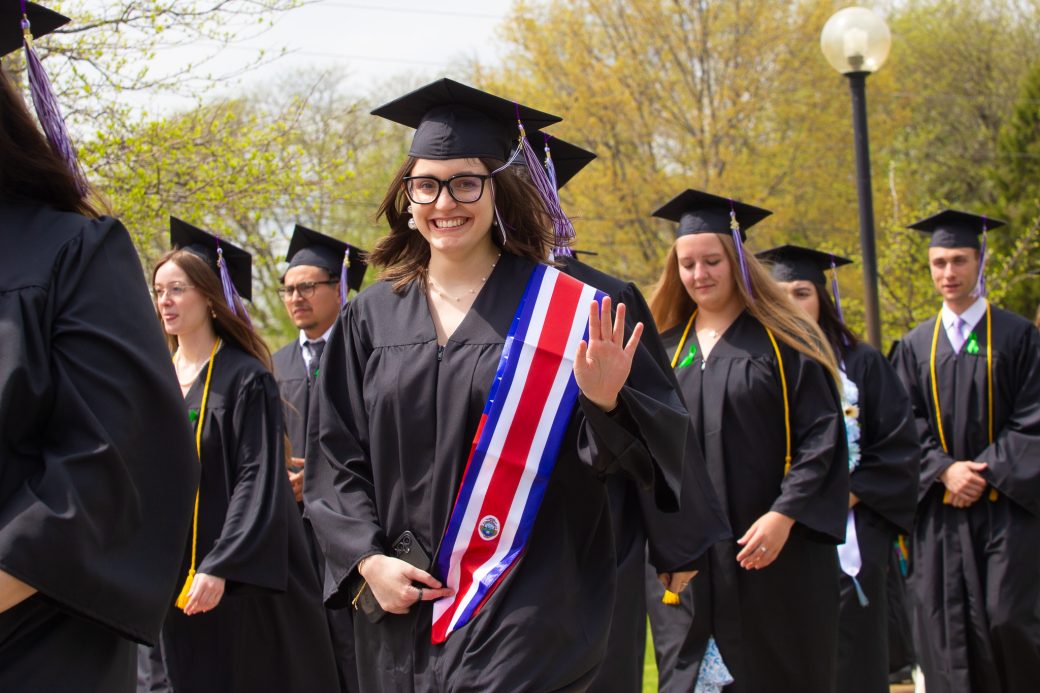 Female graduate student waving for camera with decorative stole