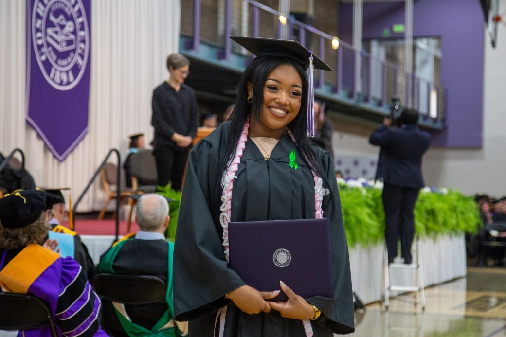 Graduate holding diploma cover and smiling off camera