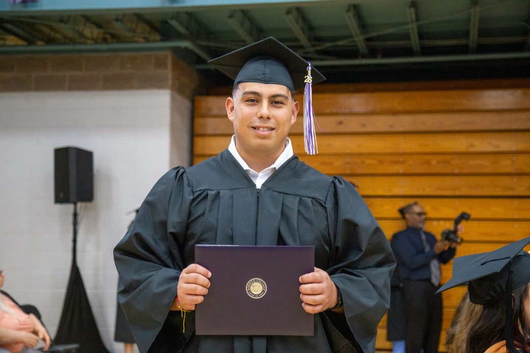 Graduate holding diploma at chest level and looking at camera