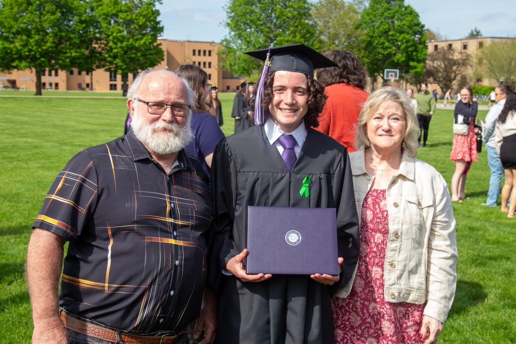 Graduate celebrating outdoors with family, friends, and faculty after commencement