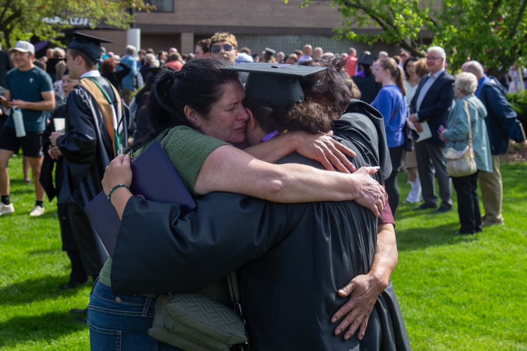 raduate surrounded by hugs from family and friends outdoors