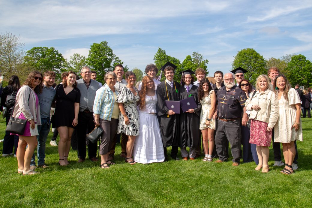 Graduate celebrating with group of family, friends, and faculty on campus lawn