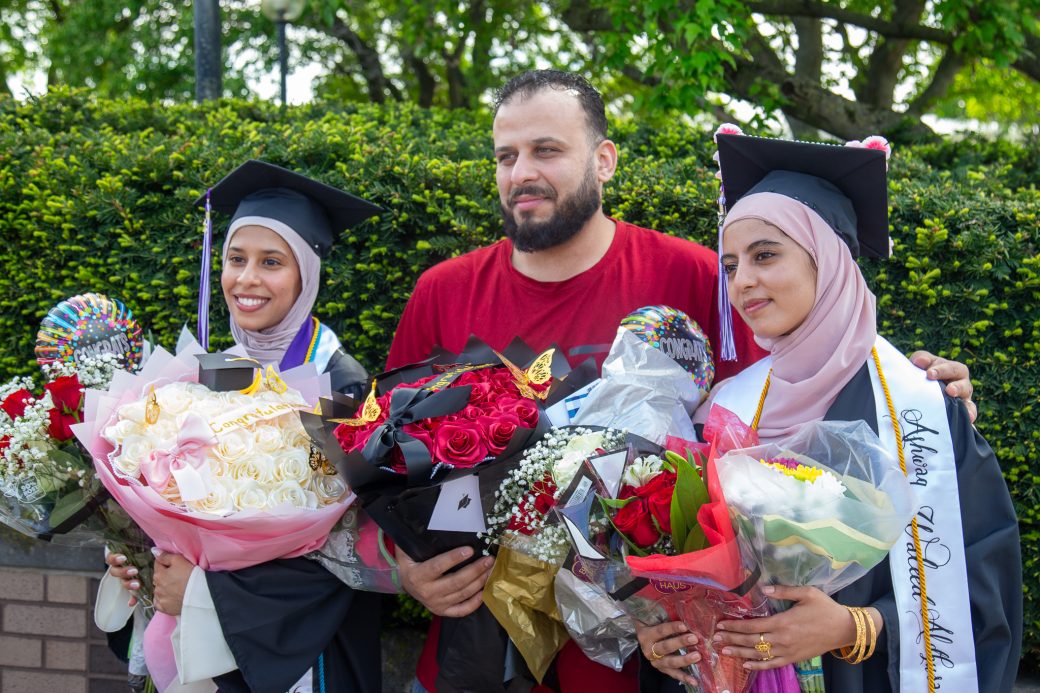 Two graduates posed with family and flowers