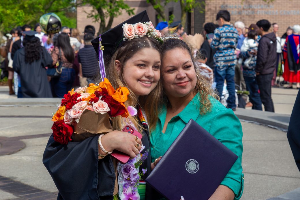 Graduate embracing family and faculty outdoors after commencement
