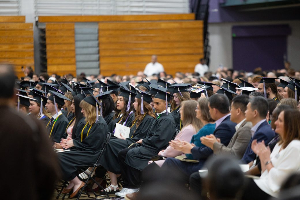 Wide view of commencement stage with graduates and faculty in regalia