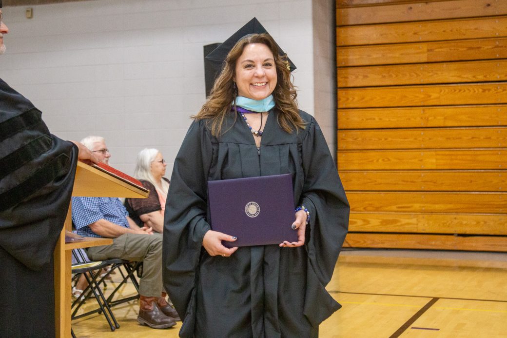 Graduate in cap and gown holding diploma cover