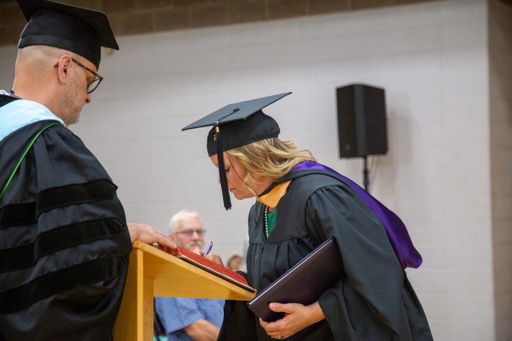 Graduate writing in book following diploma presentation
