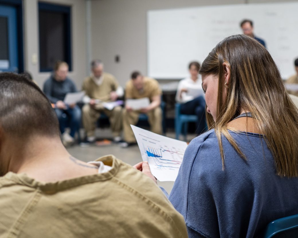 a student studying a paper, part of a ring of students, some wearing jail clothes