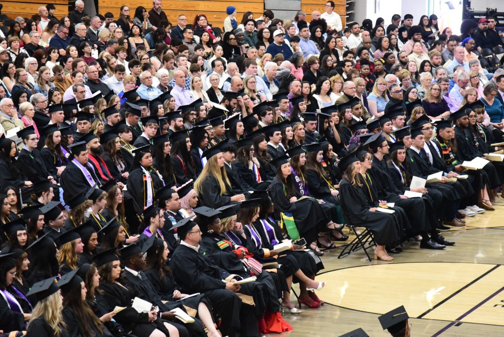 Rows of graduates facing the stage with a full audience in attendance at Goshen College commencement