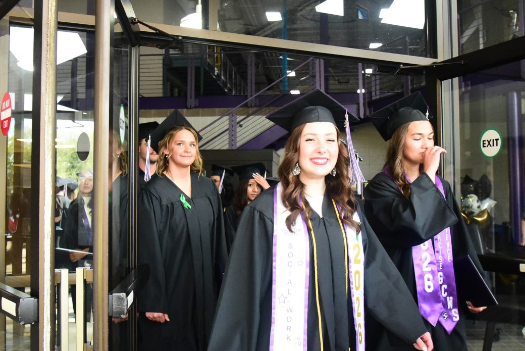 Students exiting building through doorway in caps and gowns