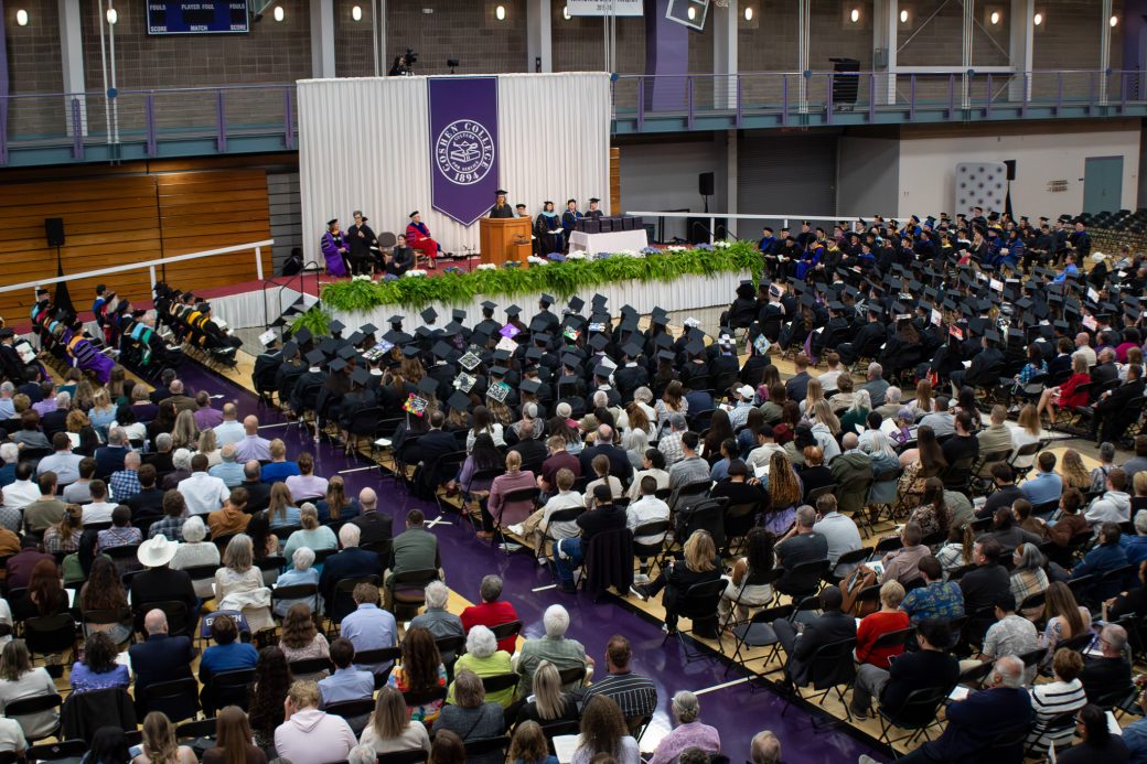 Graduates seated in rows with audience members behind them during commencement at Goshen College