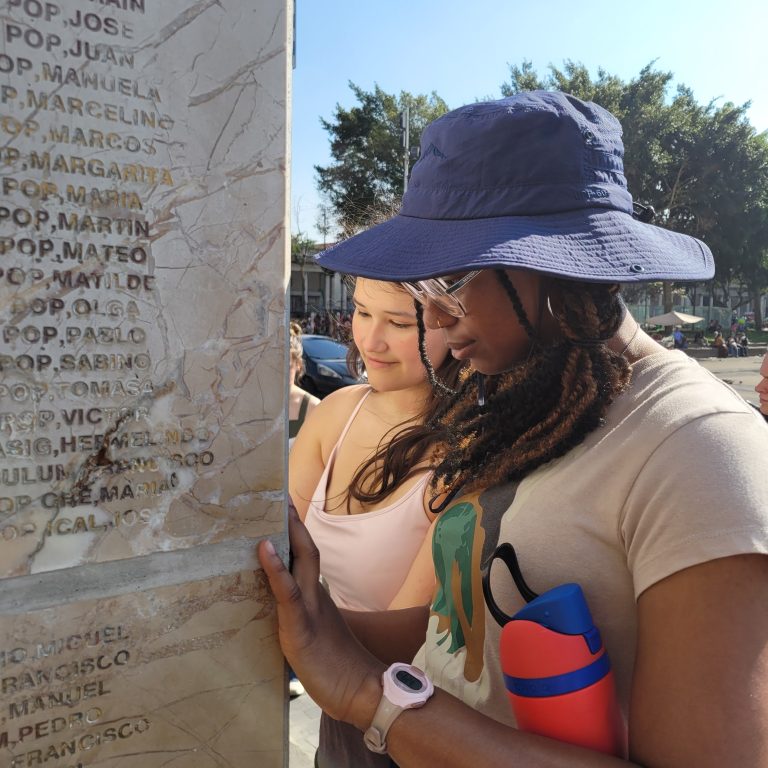 Two young women reading names etched into a stone pillar.