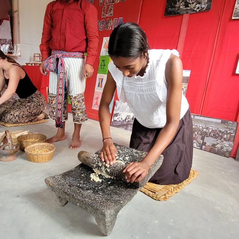 A person kneeling and grind corn with a stone.